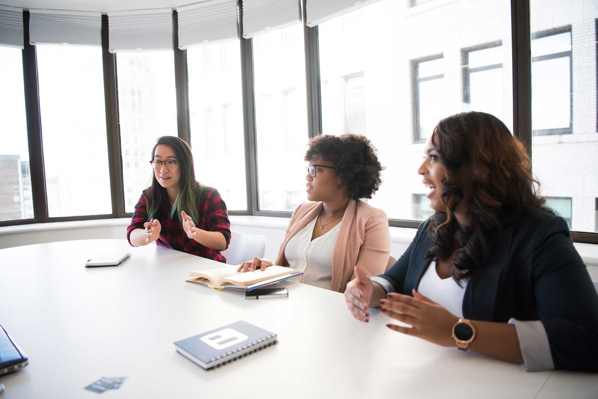 three women sitting in bright conference room at table speaking